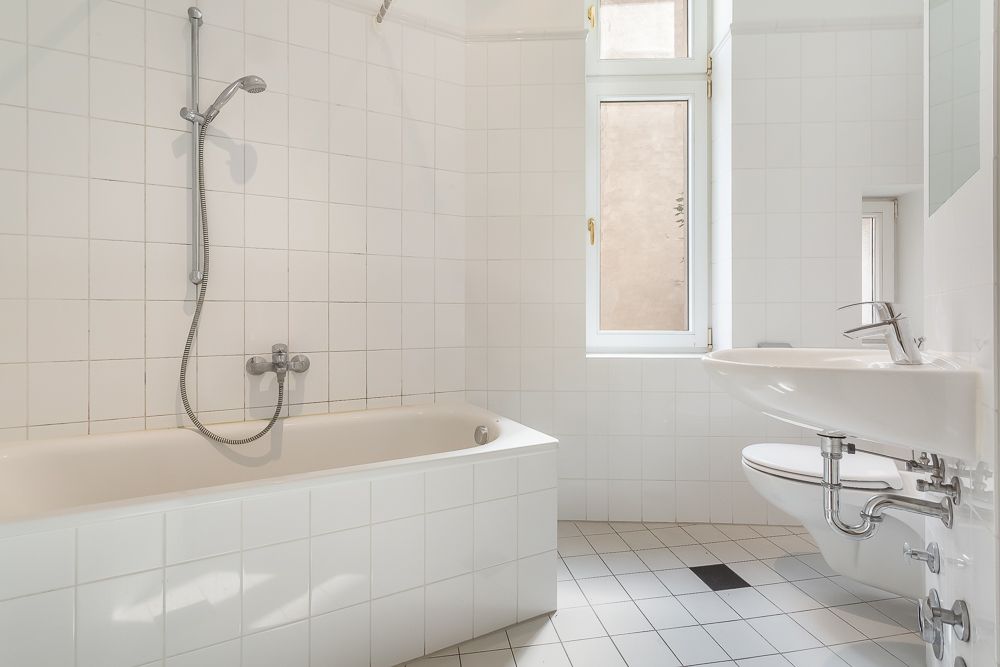 Helles Badezimmer mit Badewanne, Dusche, Fenster, Waschbecken und Toilette.