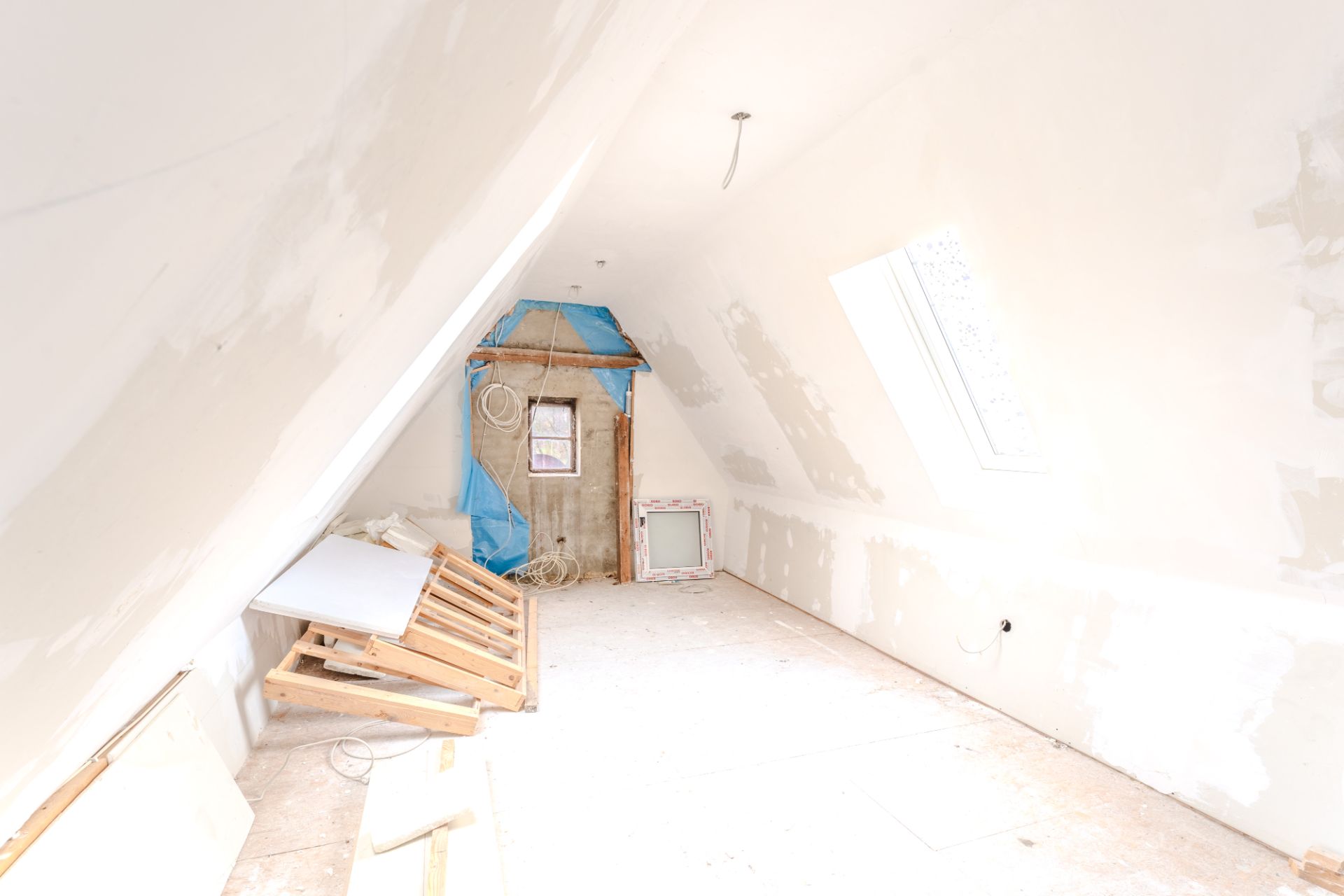 Ausgebauter Dachboden mit schrägen Wänden und Baumaterialien auf dem Boden.