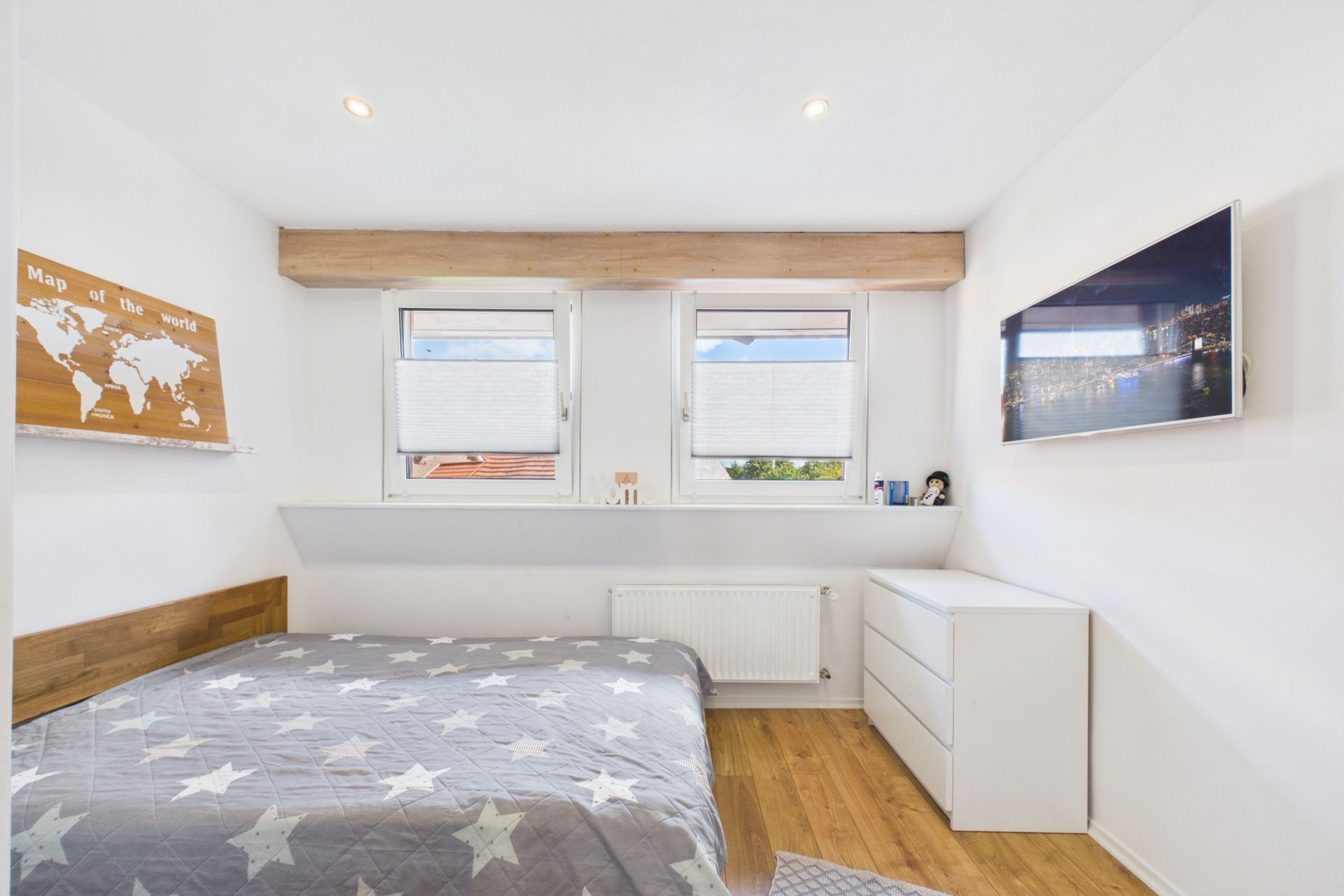Helles Schlafzimmer mit Doppelbett, Kommode, Wandkarte und Fernseher an der Wand.
