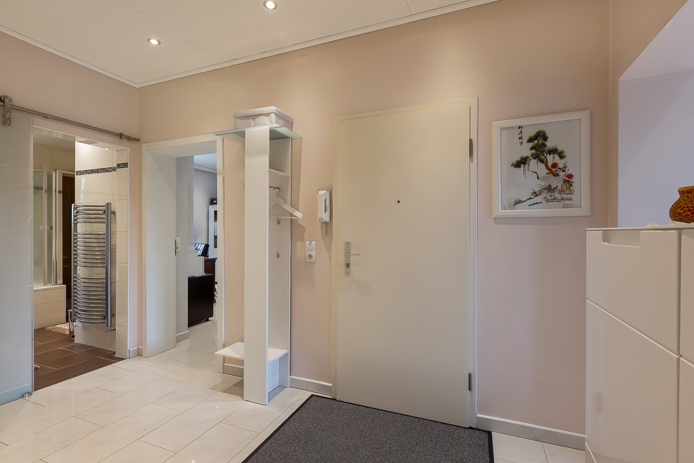 Heller Flur mit Garderobe, weißer Tür, Fliesenboden und Bild an der Wand.