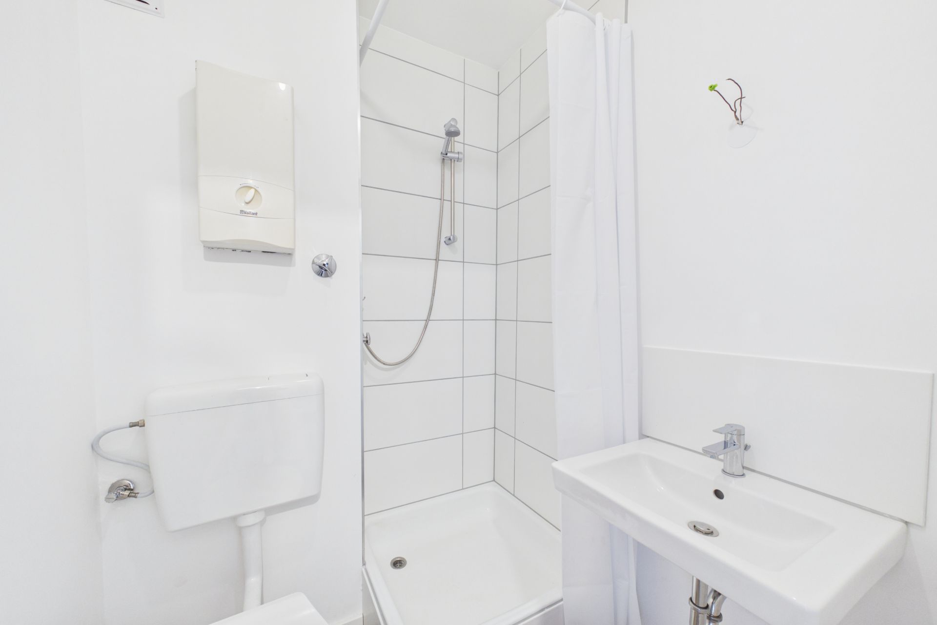Kleines, weißes Badezimmer mit Dusche, WC und Waschbecken.