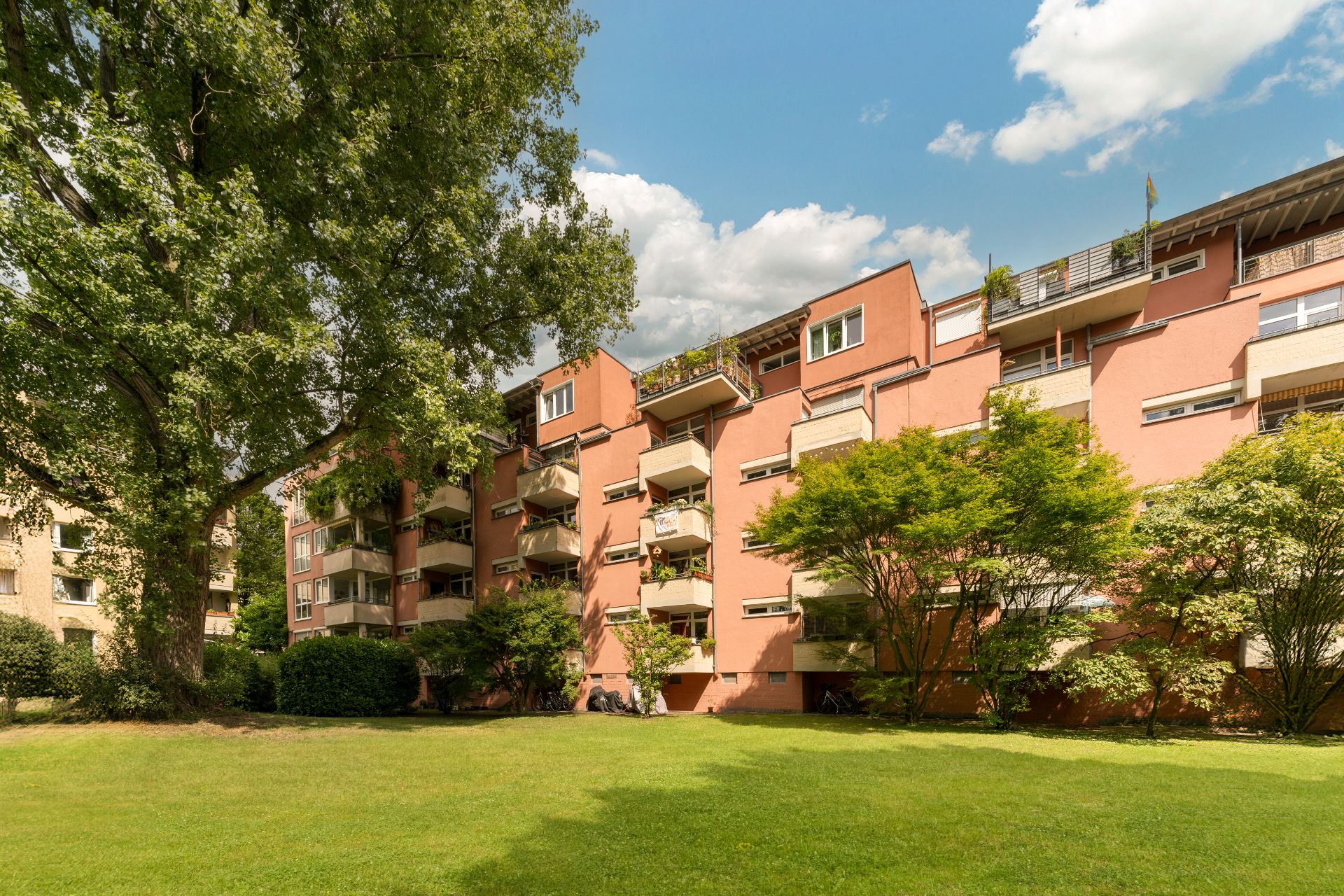 Mehrfamilienhaus mit Balkonen, umgeben von Bäumen und einer großen Rasenfläche.