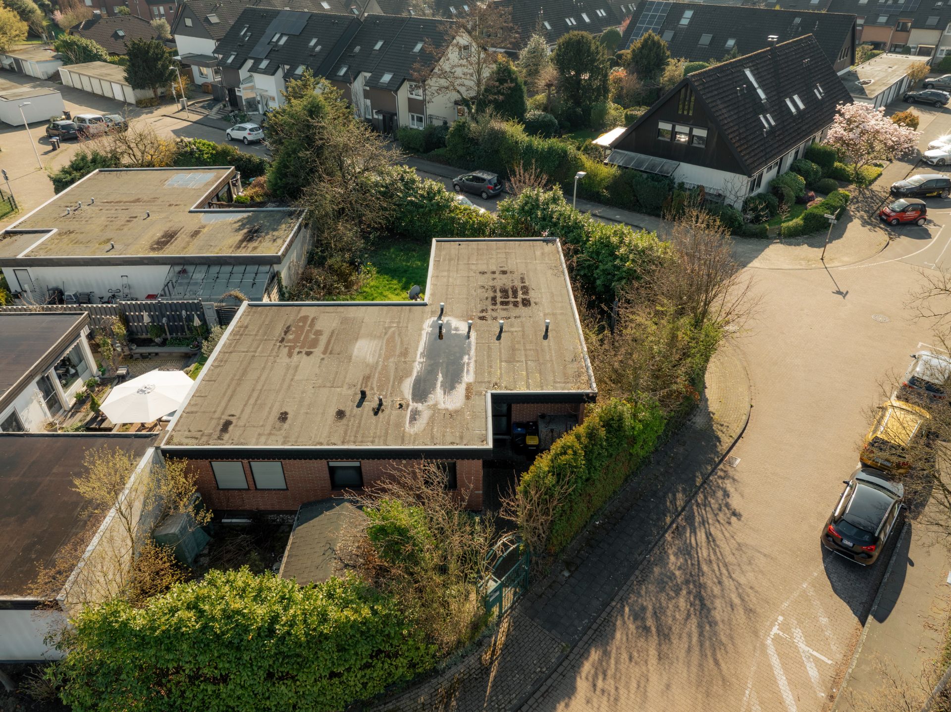 Luftaufnahme eines Flachdachhauses an einer ruhigen Wohnstraße mit umliegenden Gärten.