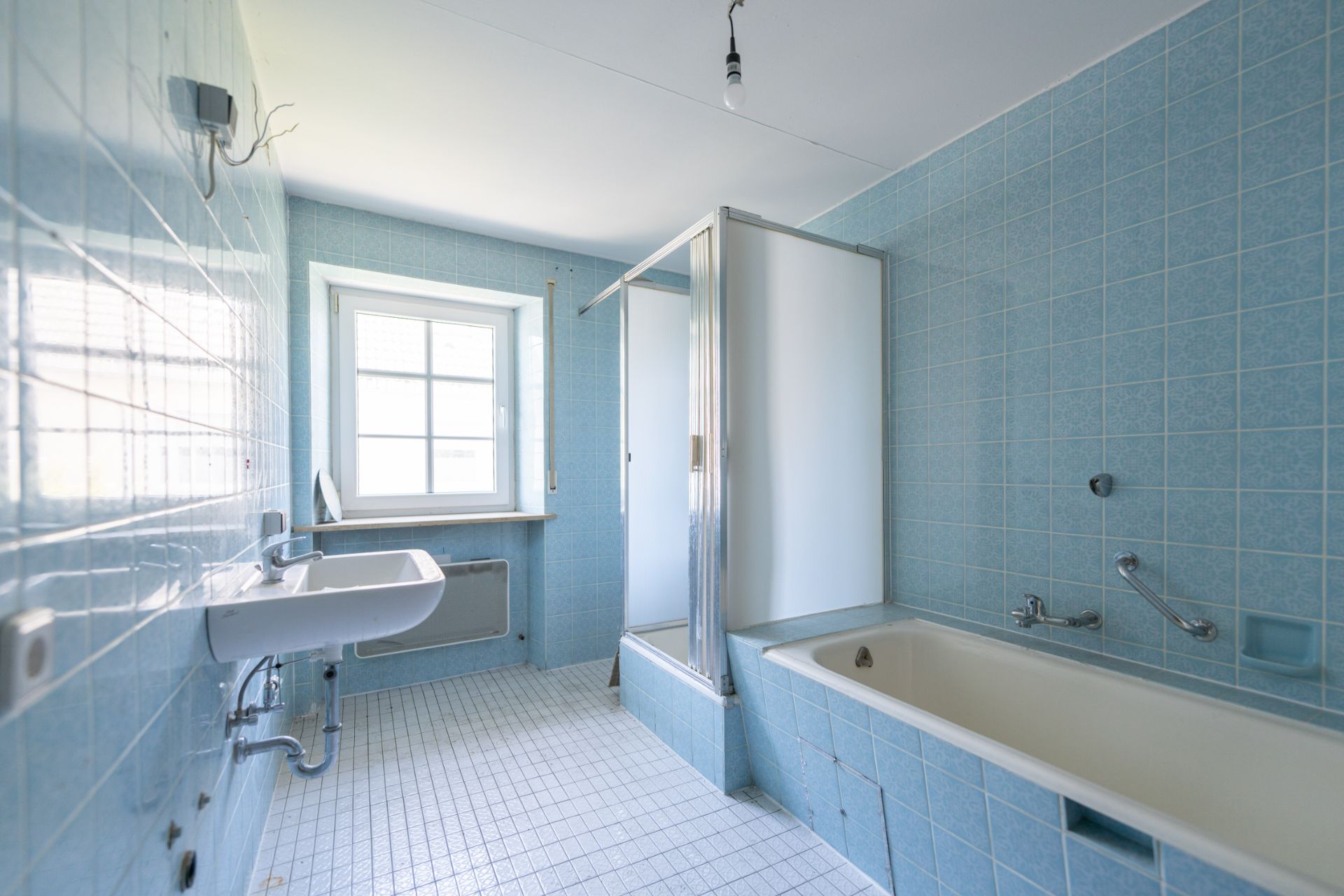 Helles Badezimmer mit blauen Fliesen, Badewanne, Dusche, Waschbecken und Fenster.