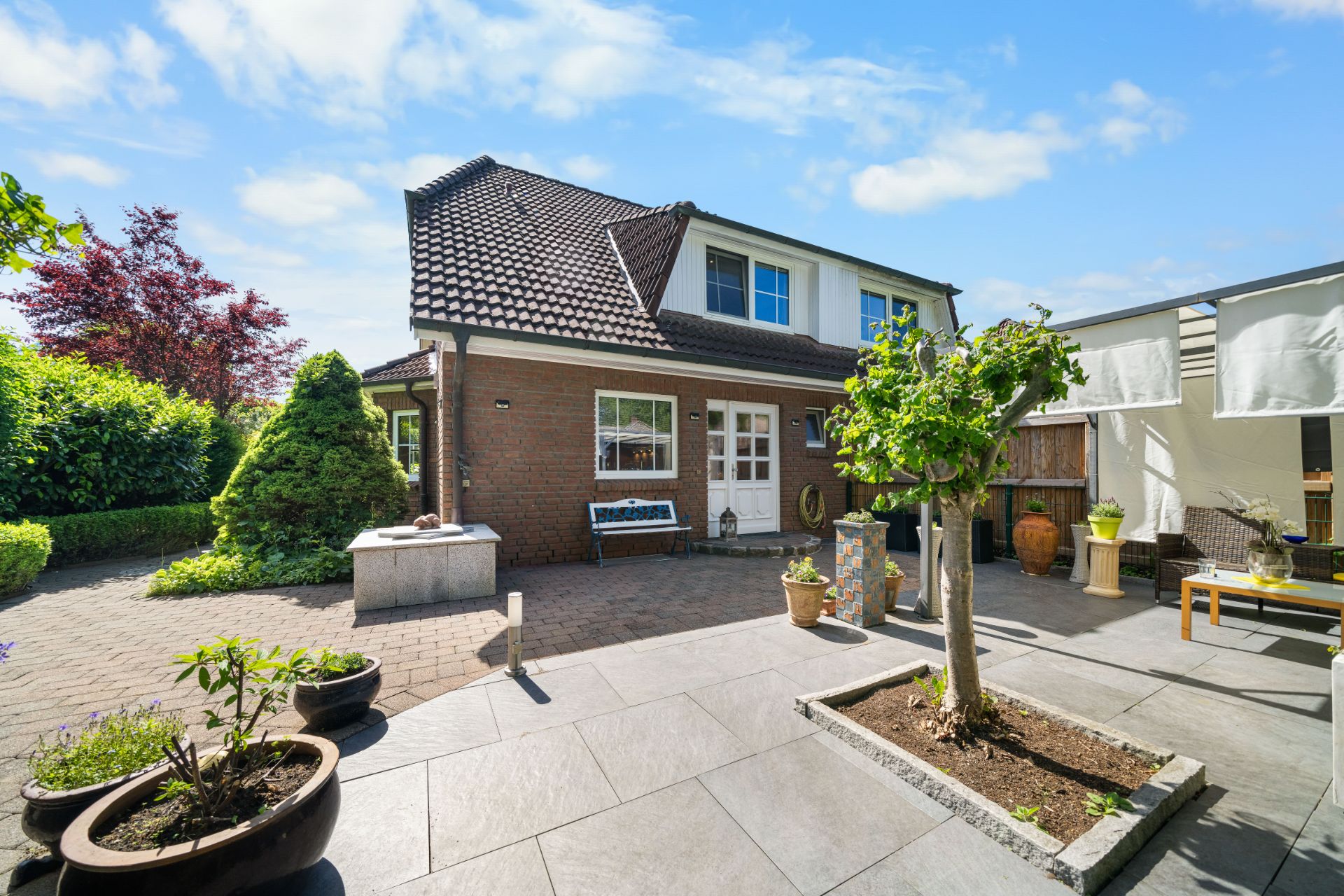 Gepflegter Gartenhof mit jungen Bäumen, Töpfen und Sitzbereich vor einem Einfamilienhaus.