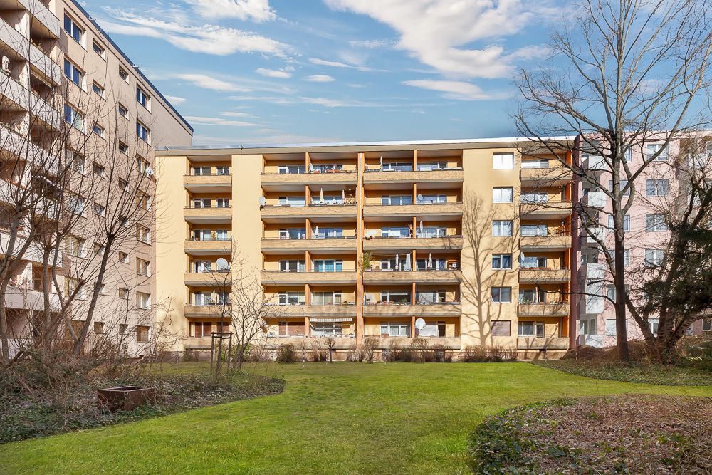 Mehrstöckiges Wohngebäude mit Balkonen und Rasenfläche im Vordergrund.