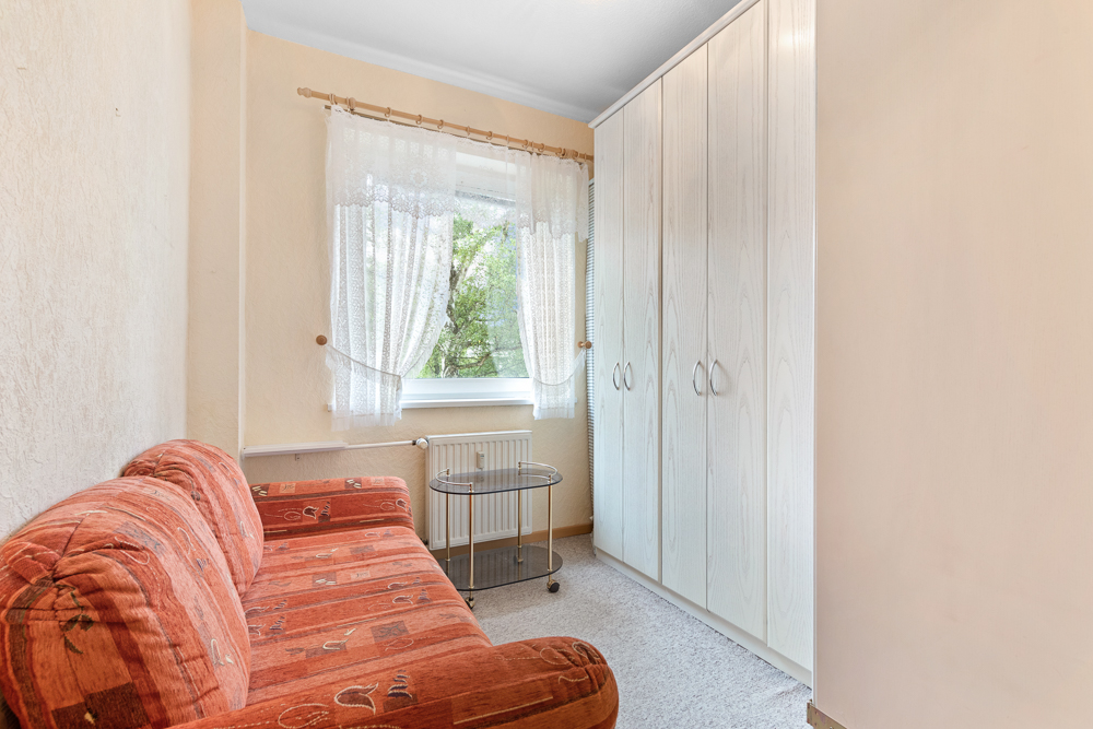 Kleines Zimmer mit rotem Sofa, weißem Kleiderschrank und Fenster mit Gardinen.