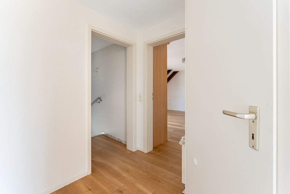 Flur mit Holzboden, offene Türen zu zwei Zimmern und Treppenaufgang.
