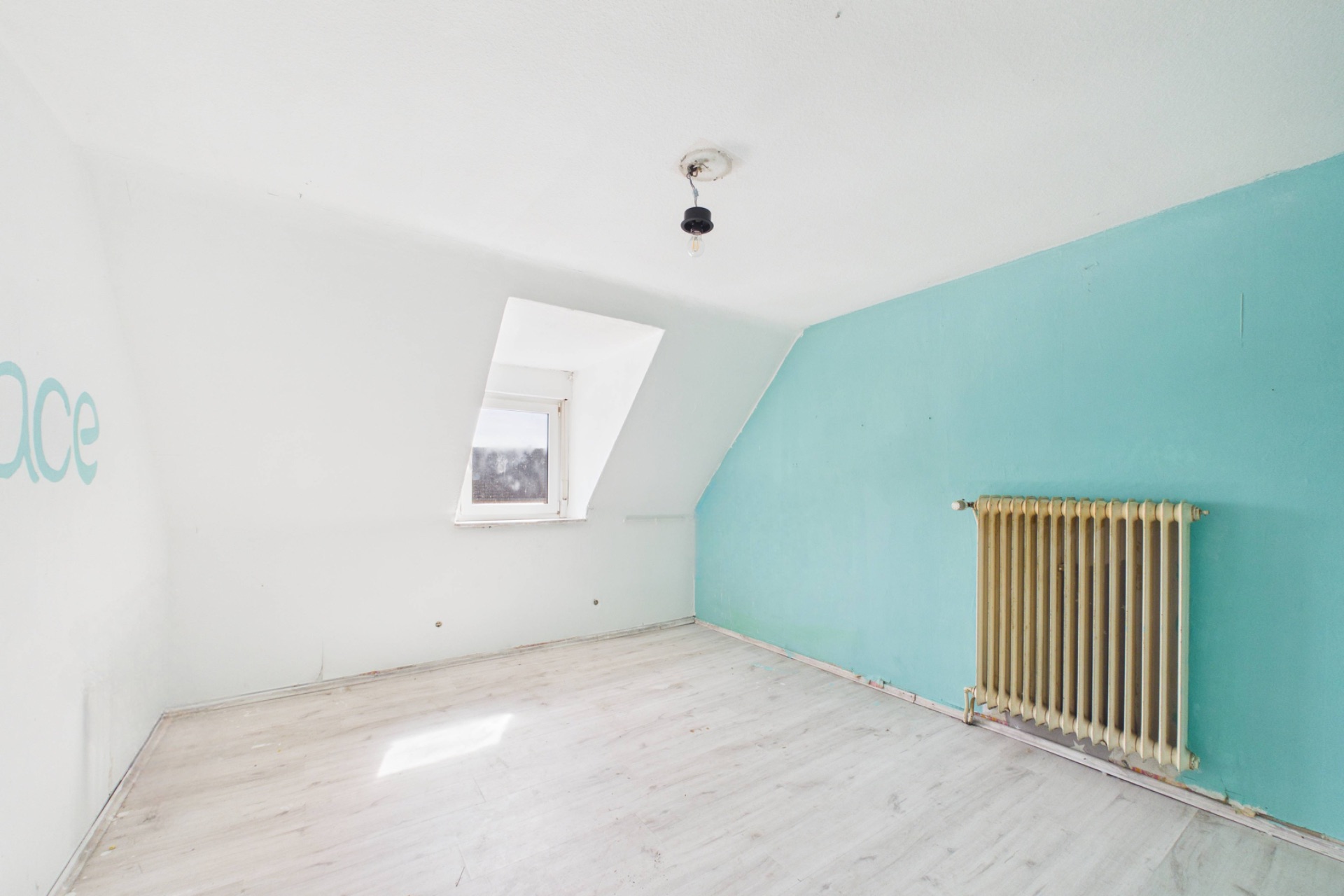 Leeres Zimmer mit türkisfarbener Wand, Fenster und Heizkörper.