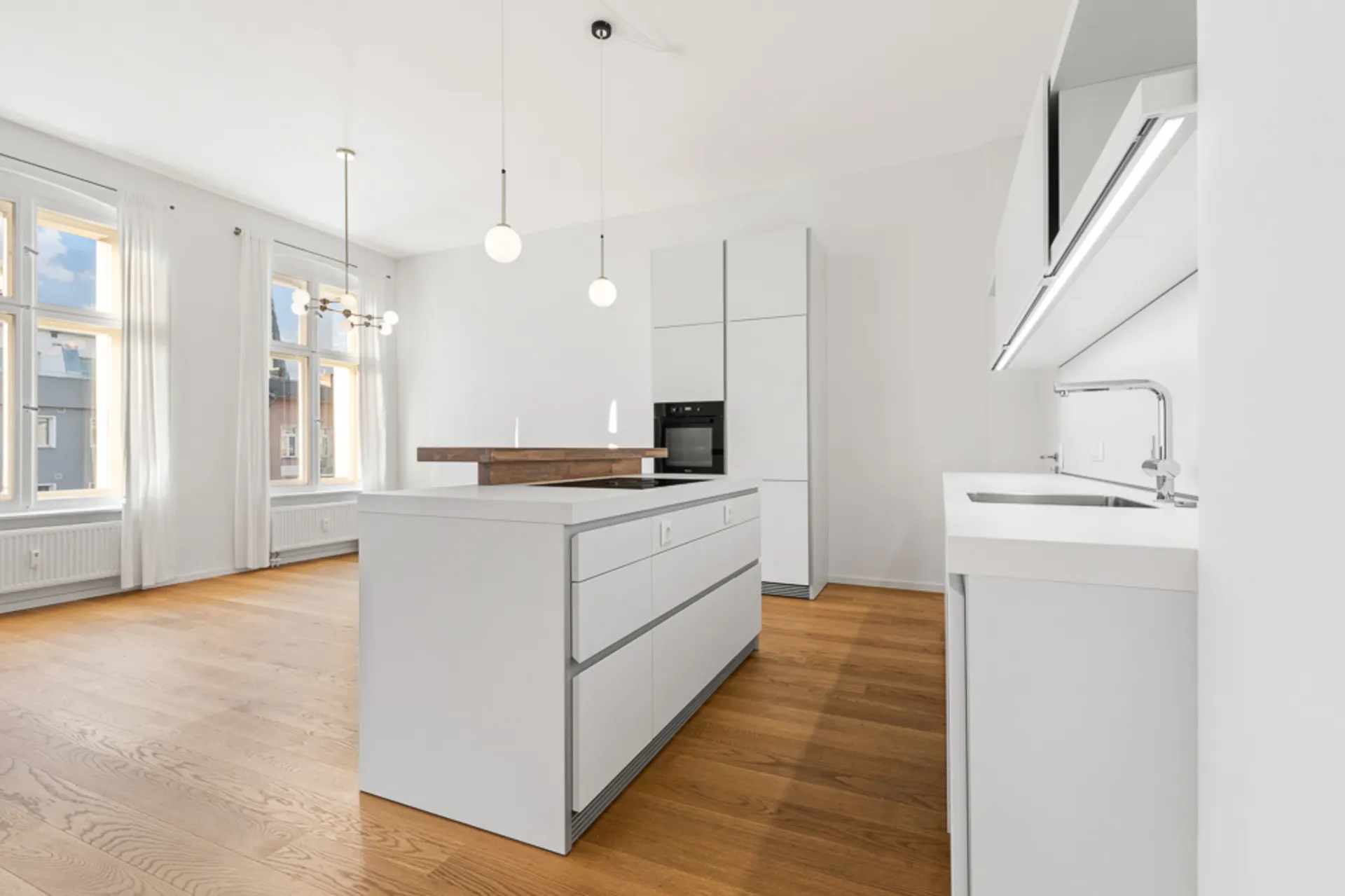Moderne, helle Küche mit Kücheninsel, weißen Schränken und Holzboden in einem offenen Raum.