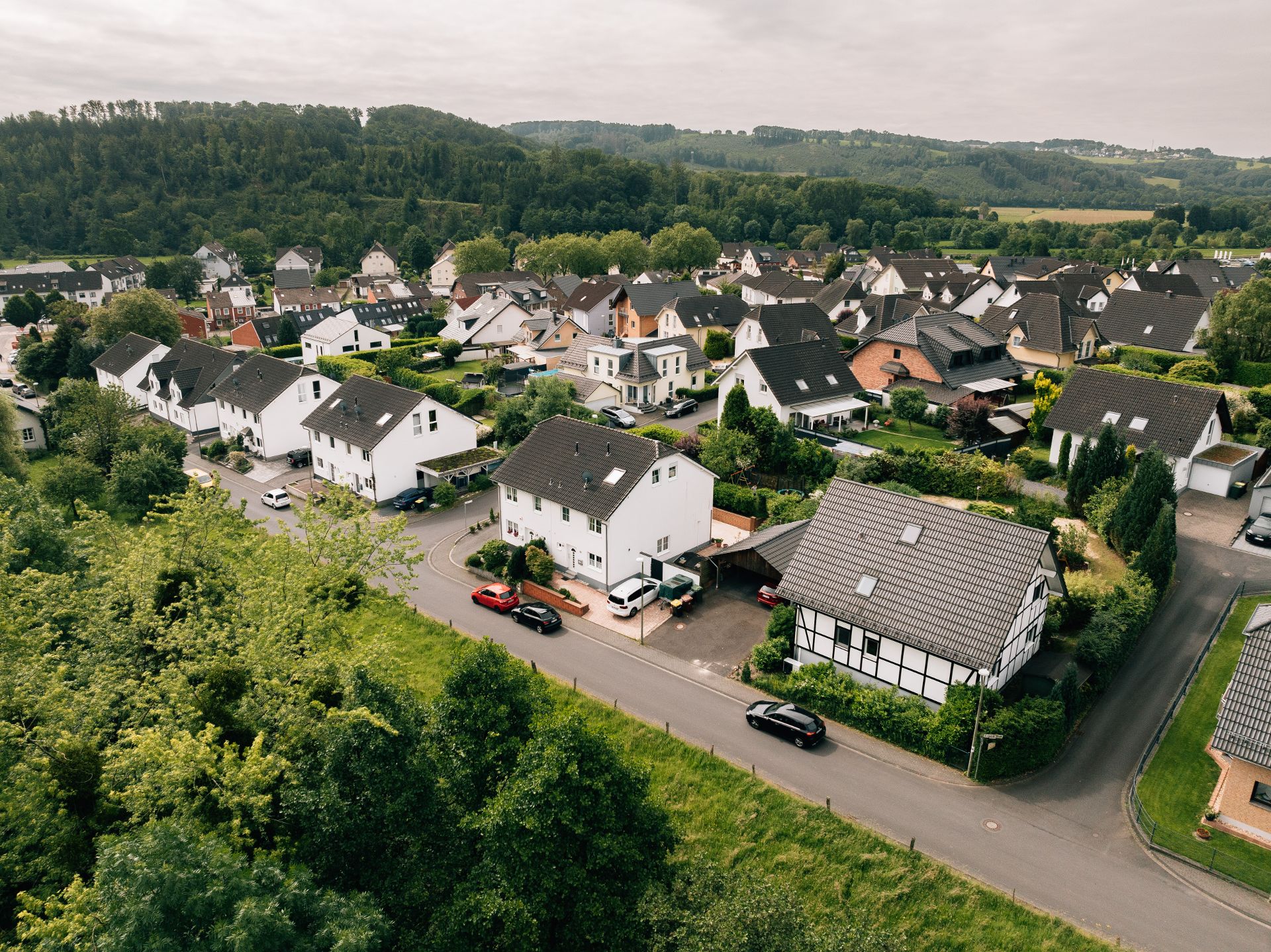 Luftaufnahme eines Wohngebiets mit Einfamilienhäusern, Straßen und viel Grün.