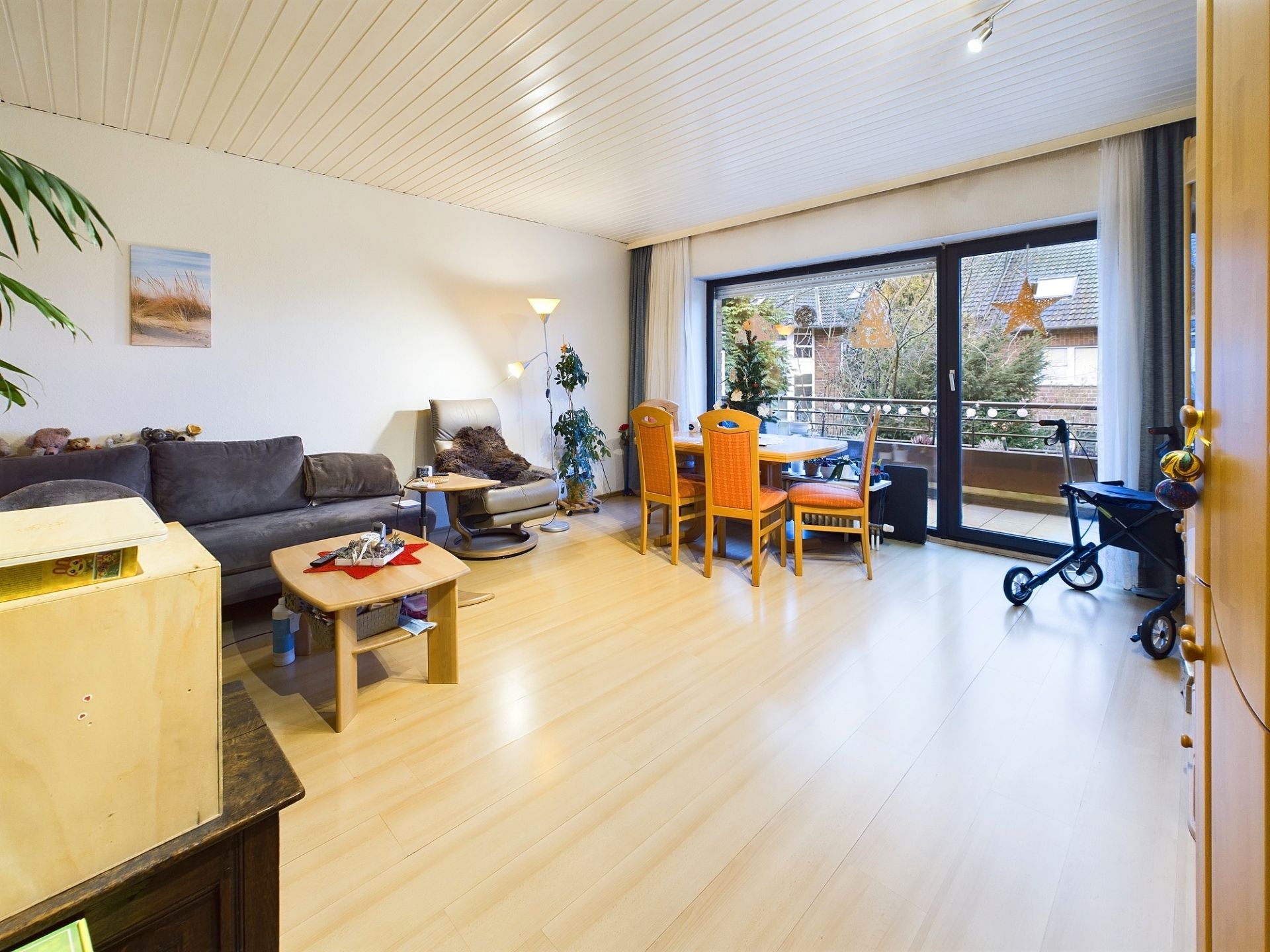 Helles Wohnzimmer mit Sofa, Esstisch, Kinderwagen und Zugang zu einem Balkon.