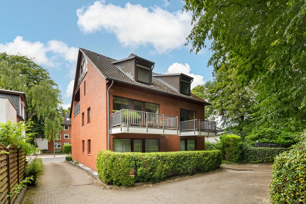 Rotes Mehrfamilienhaus mit Balkonen, Auffahrt und umgeben von Bäumen und Hecken.