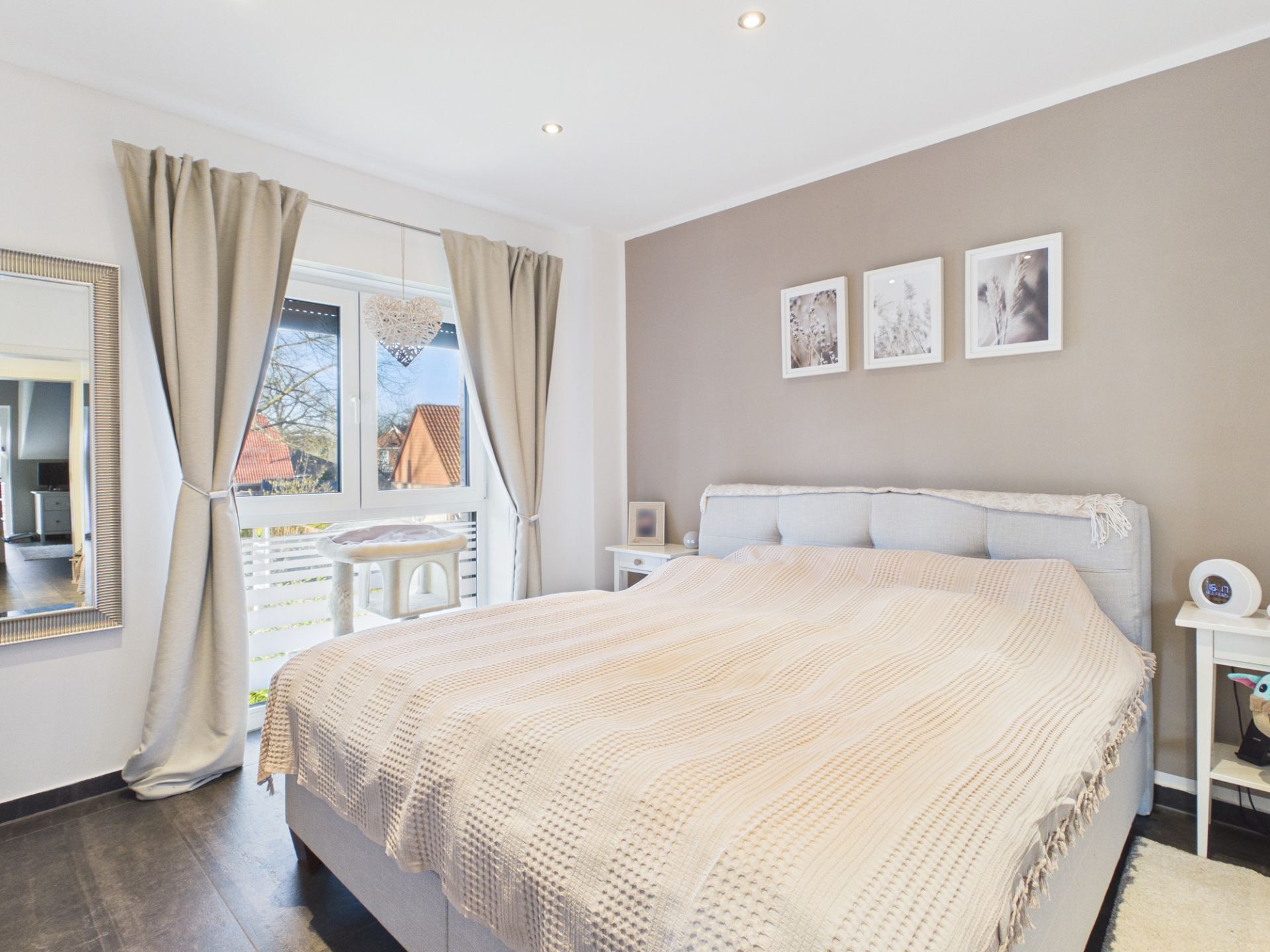 Helles Schlafzimmer mit Doppelbett, Nachttischen, großem Fenster und beigen Vorhängen.
