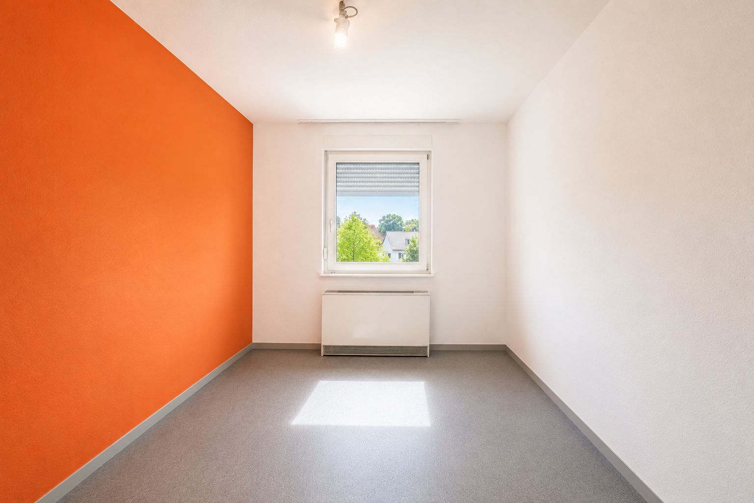 Leerer Raum mit orangefarbener Wand, Fenster und grauem Boden.