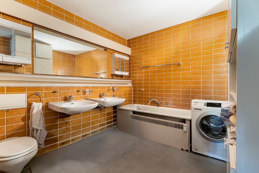Badezimmer mit orangefarbenen Fliesen, zwei Waschbecken, Badewanne, Waschmaschine und großem Spiegel.