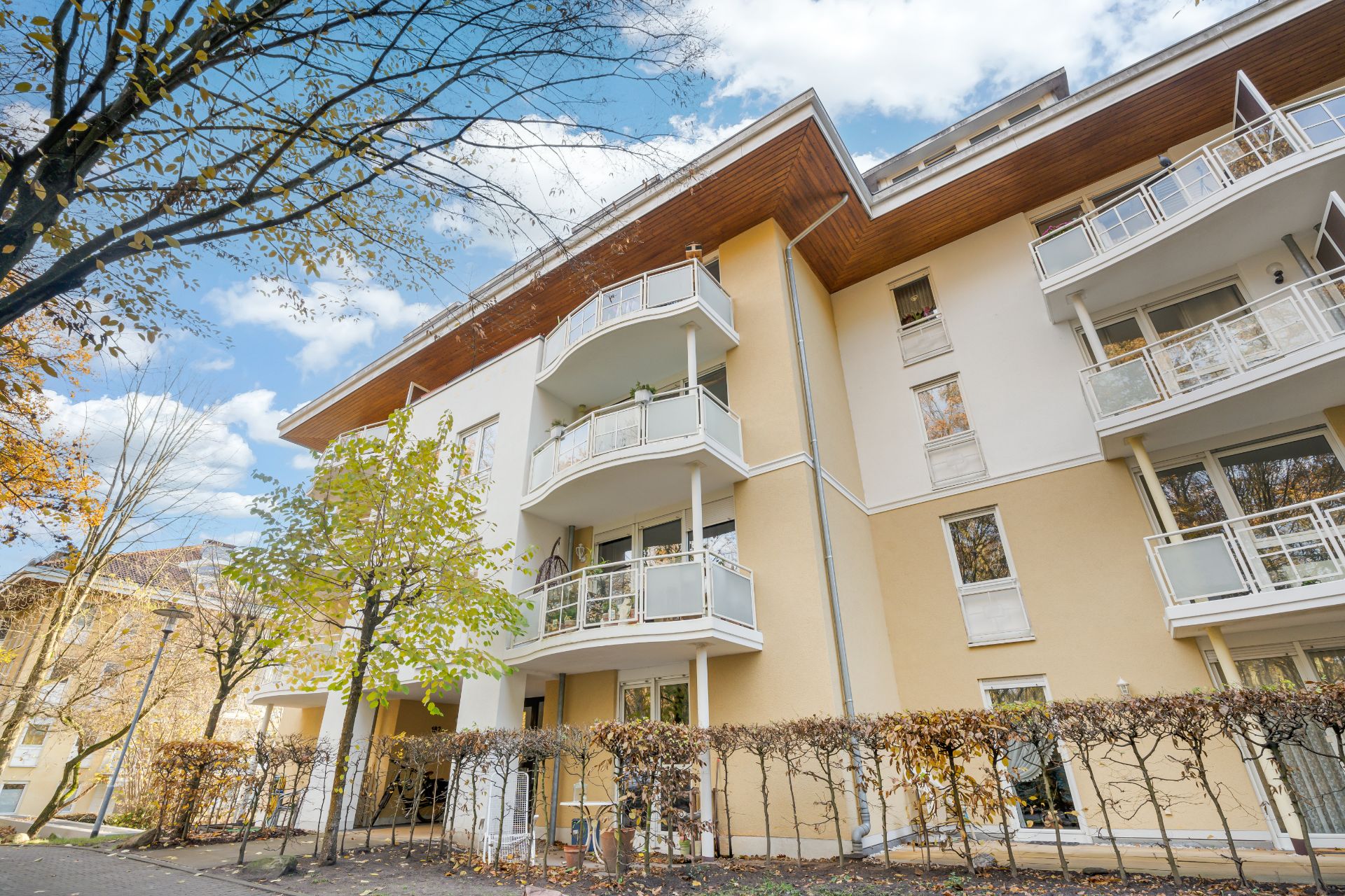 Mehrstöckiges Wohnhaus mit mehreren Balkonen und hellgelber Fassade im Herbst.