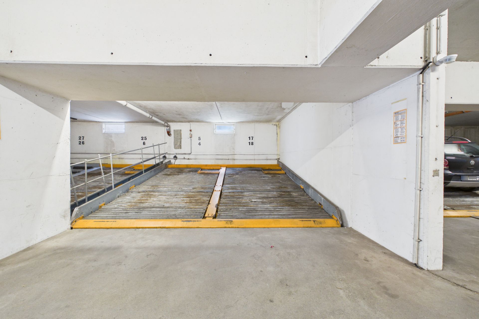 Innenansicht einer Tiefgarage mit Parkplätzen und weißen Wänden.