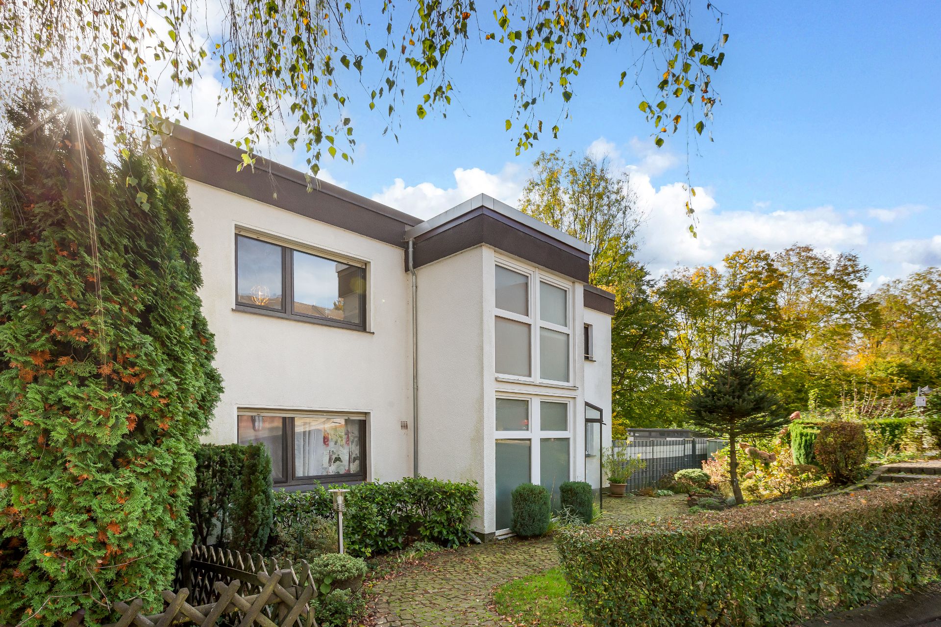 Zweistöckiges, modernes Wohnhaus mit großen Fenstern und Garten bei sonnigem Wetter.