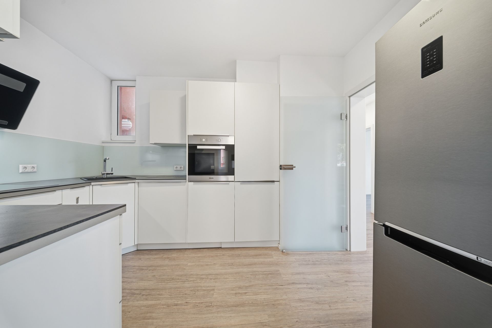 Moderne Küche mit weißen Schränken, Einbauherd, großem Kühlschrank und Holzfußboden.