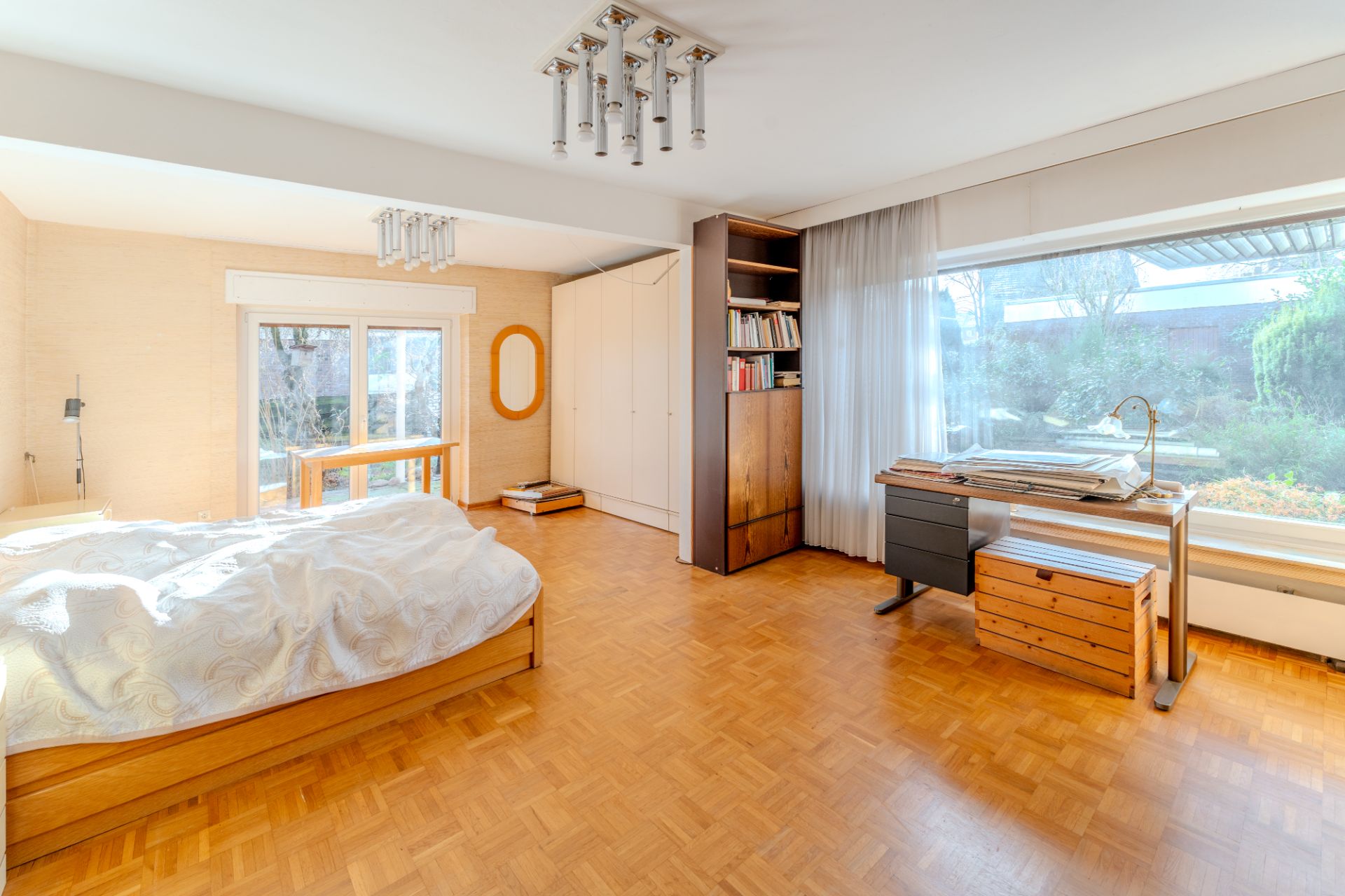 Helles Schlafzimmer mit Doppelbett, Schreibtisch, Schrank und großem Fenster mit Blick in den Garten.
