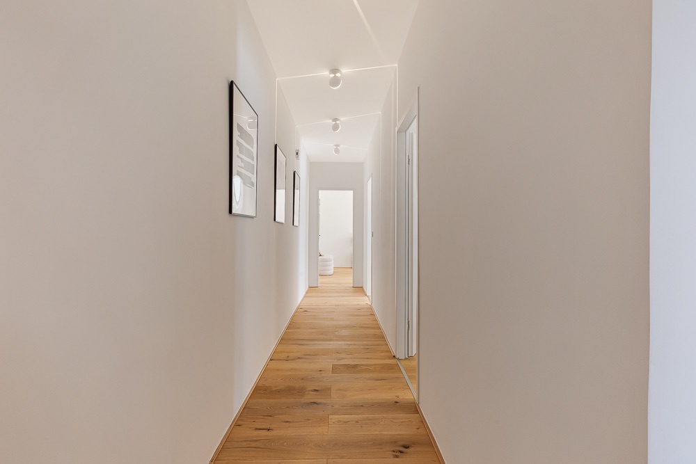 Heller Flur mit Holzboden, weißen Wänden und mehreren Bildern an der Wand.