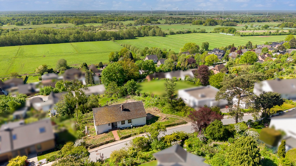 Luftaufnahme eines Einfamilienhauses mit Garten am Rand eines Wohngebiets, umgeben von Feldern.