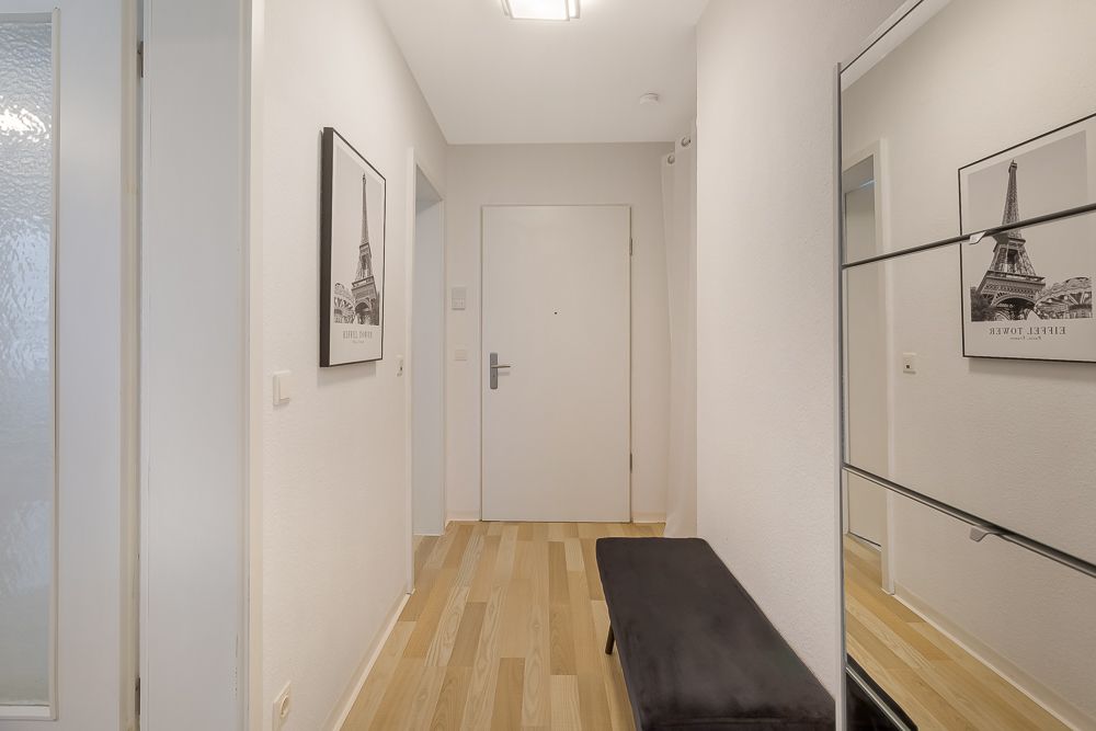 Heller Flur mit Holzboden, Bank, Spiegel und einem Bild an der Wand.