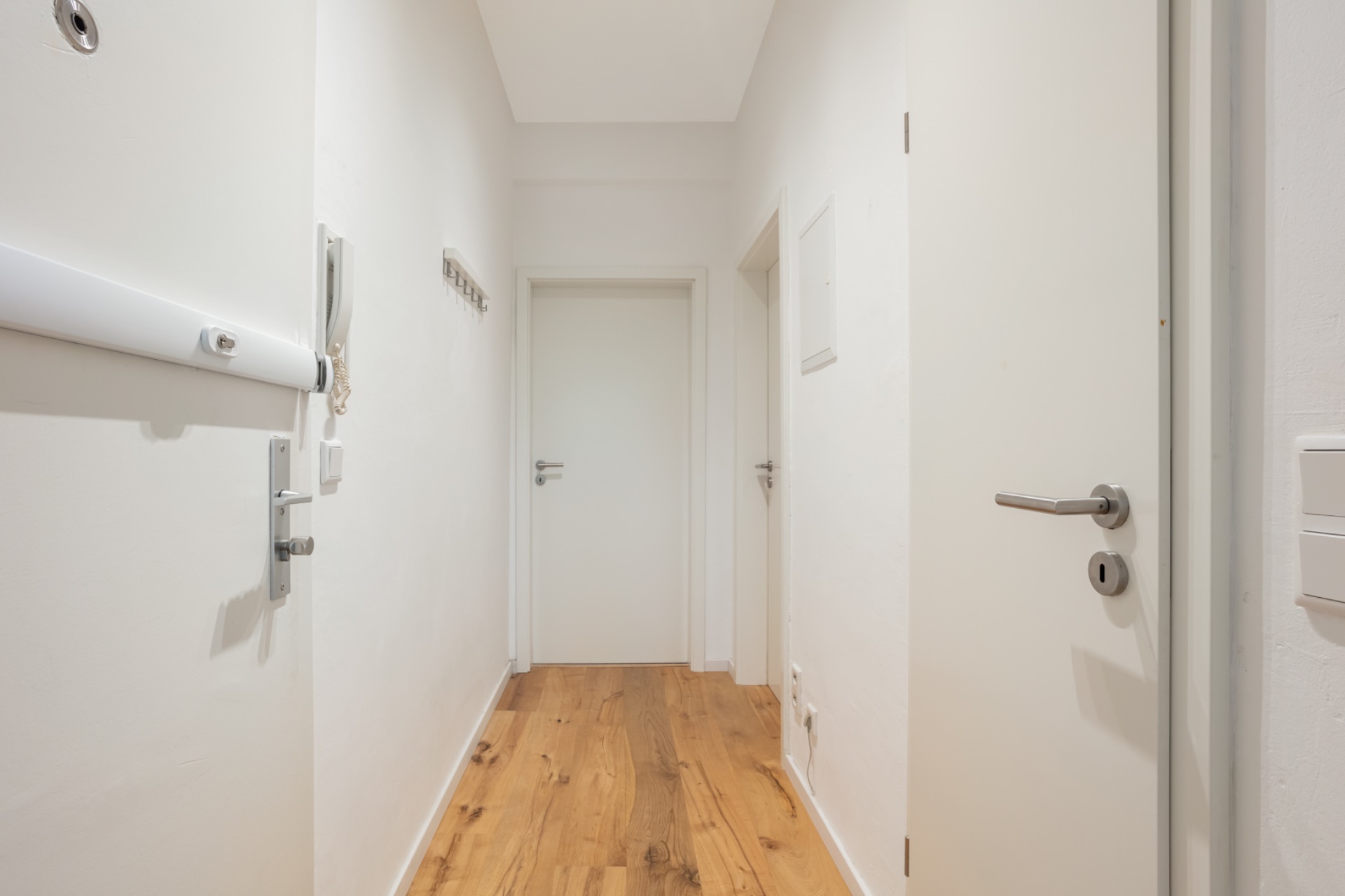 Heller Flur mit Holzboden und mehreren weißen Türen in einer Wohnung.