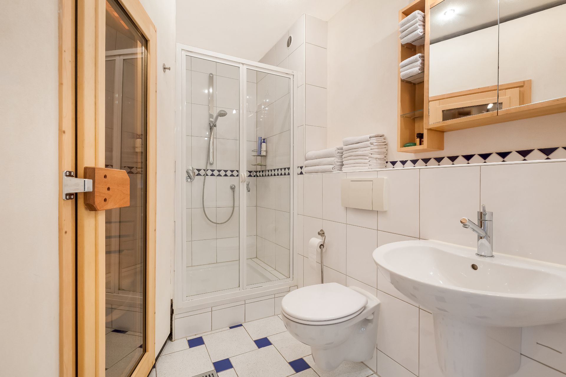 Modernes Badezimmer mit Dusche, Toilette, Waschbecken, Sauna und Handtüchern auf dem Regal.