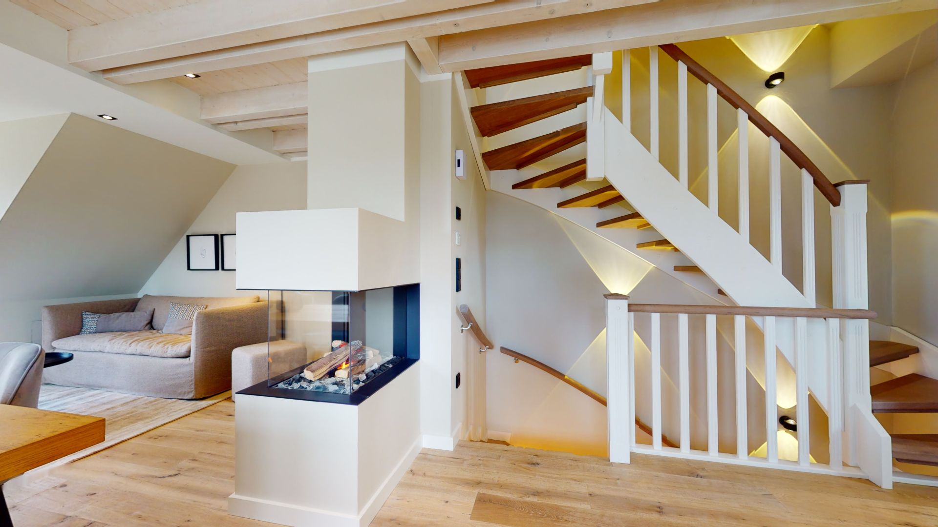 Wohnbereich mit Kamin und hölzerner Treppe, Sofa im Hintergrund.