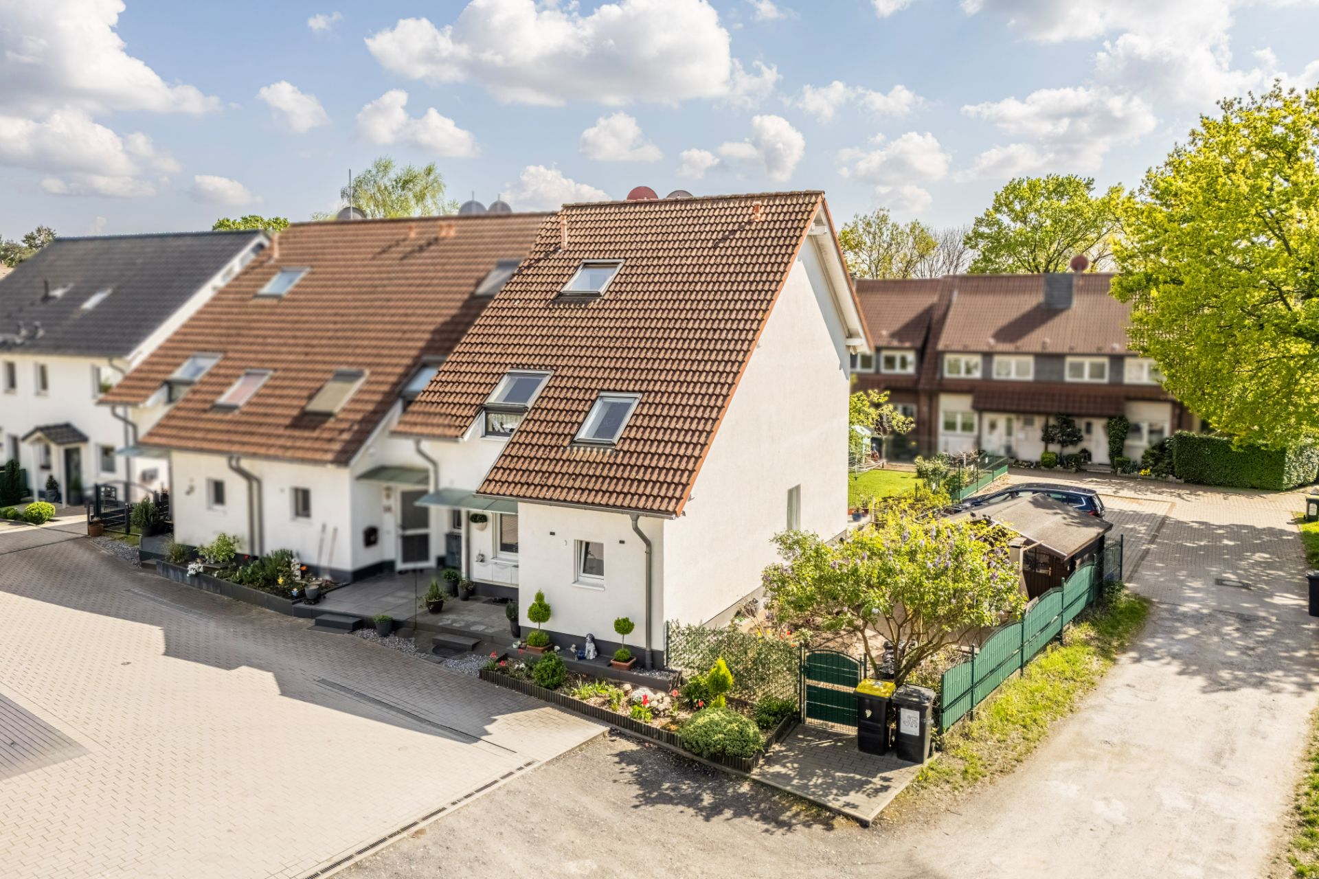 Modernes Reihenendhaus mit rotem Dach, kleinem Garten und Einfahrt, umgeben von Nachbarhäusern.