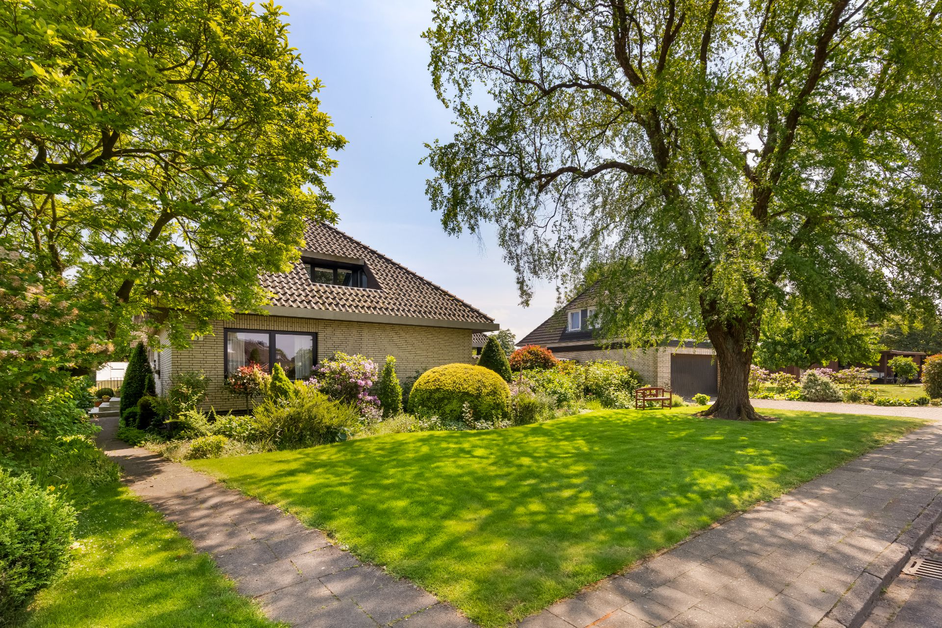 Ein Einfamilienhaus mit gepflegtem Garten, Rasenfläche und großen Bäumen an einer ruhigen Straße.