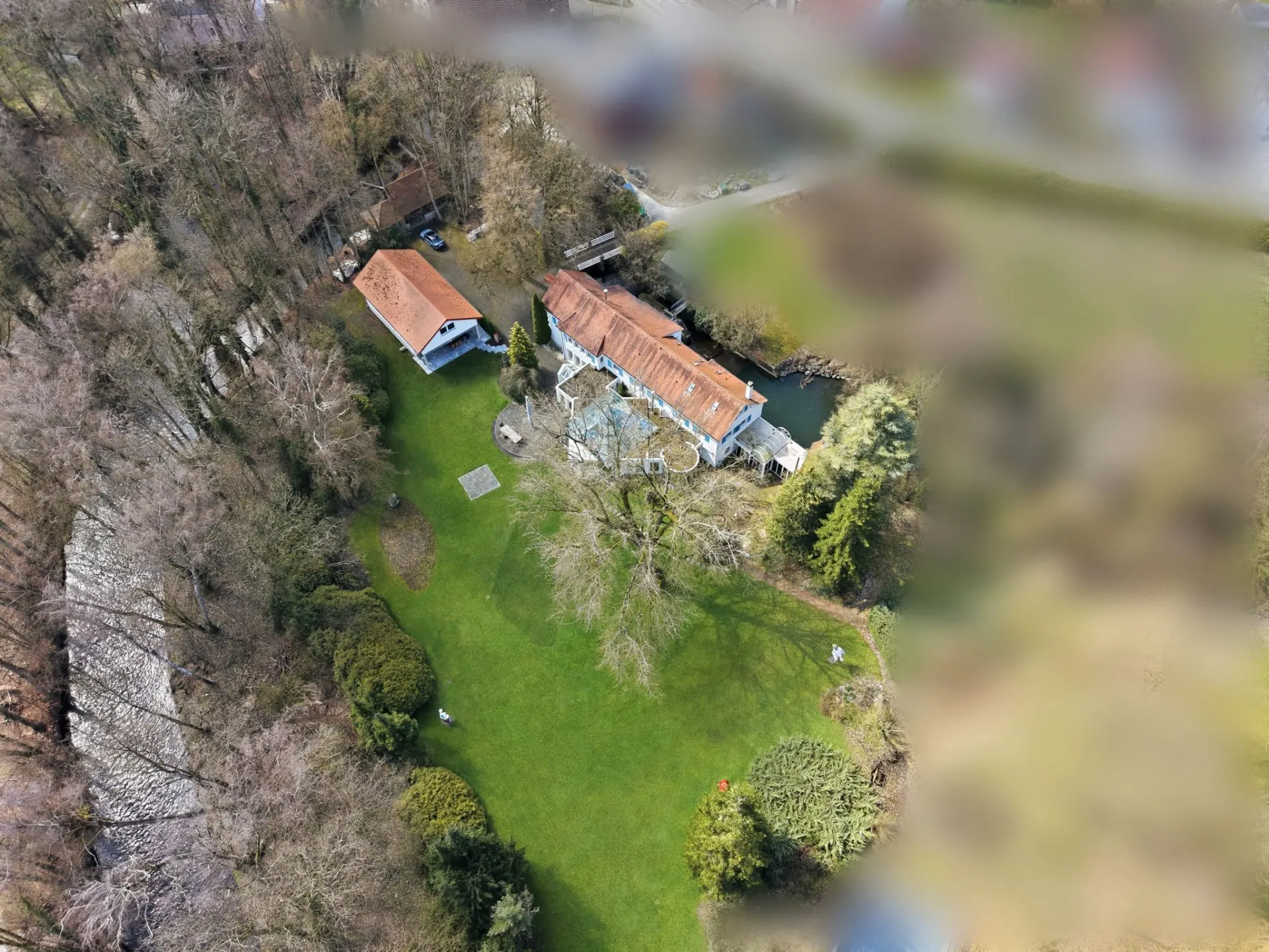 Luftaufnahme eines Hauses mit rotem Dach und großem Garten, umgeben von Bäumen.