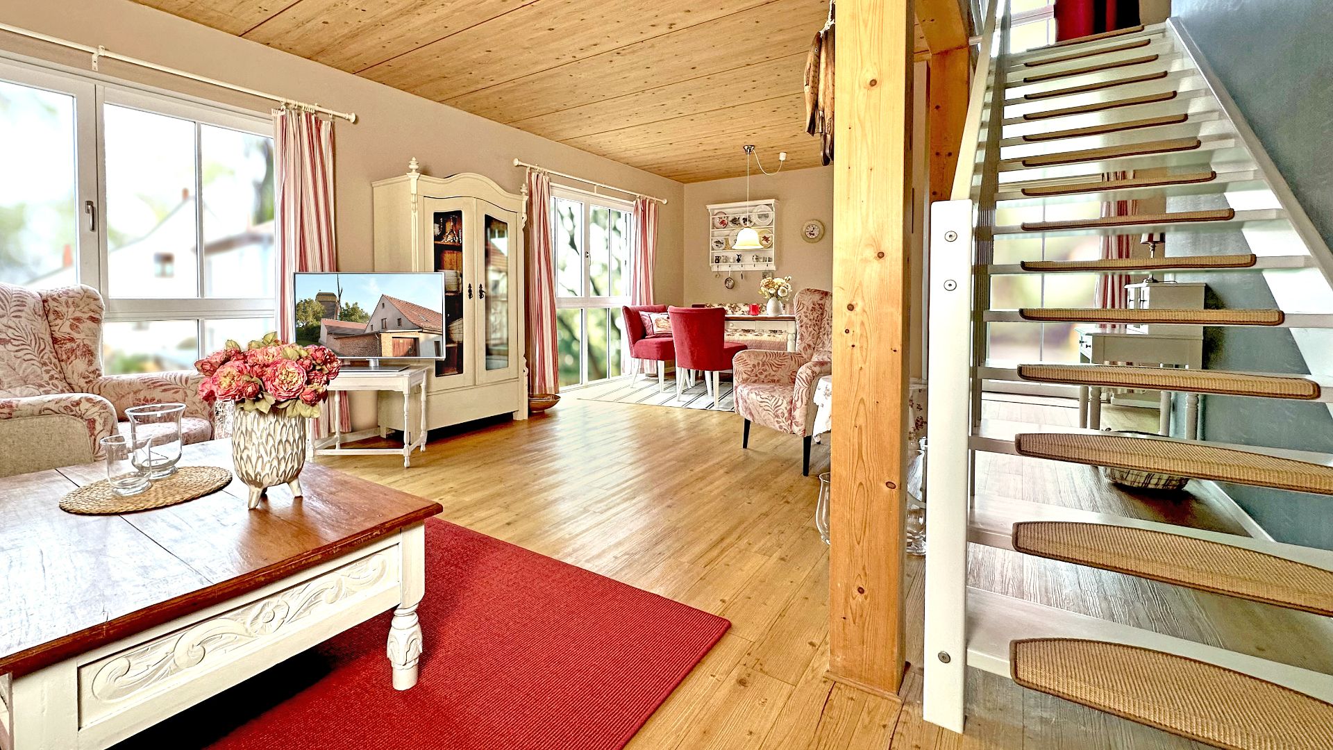 Helles Wohnzimmer mit Holzdecke, Sofas, Couchtisch, Fenster und moderner Treppe.