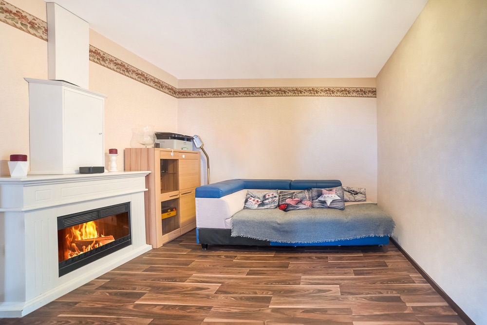 Wohnzimmer mit Ecksofa, Kamin und Holzregal auf Holzfußboden.