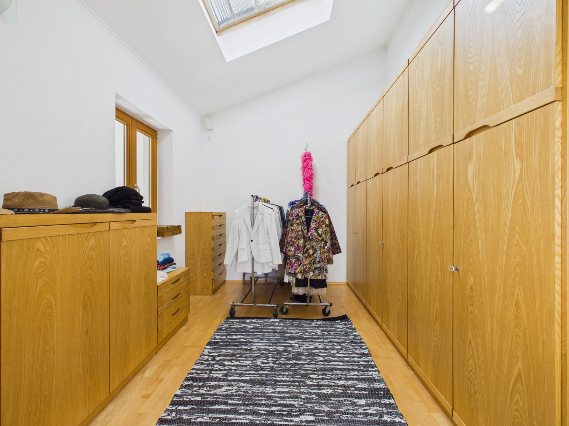 Ankleidezimmer mit Holzschränken, Kommoden und Kleiderständern unter Dachfenster.