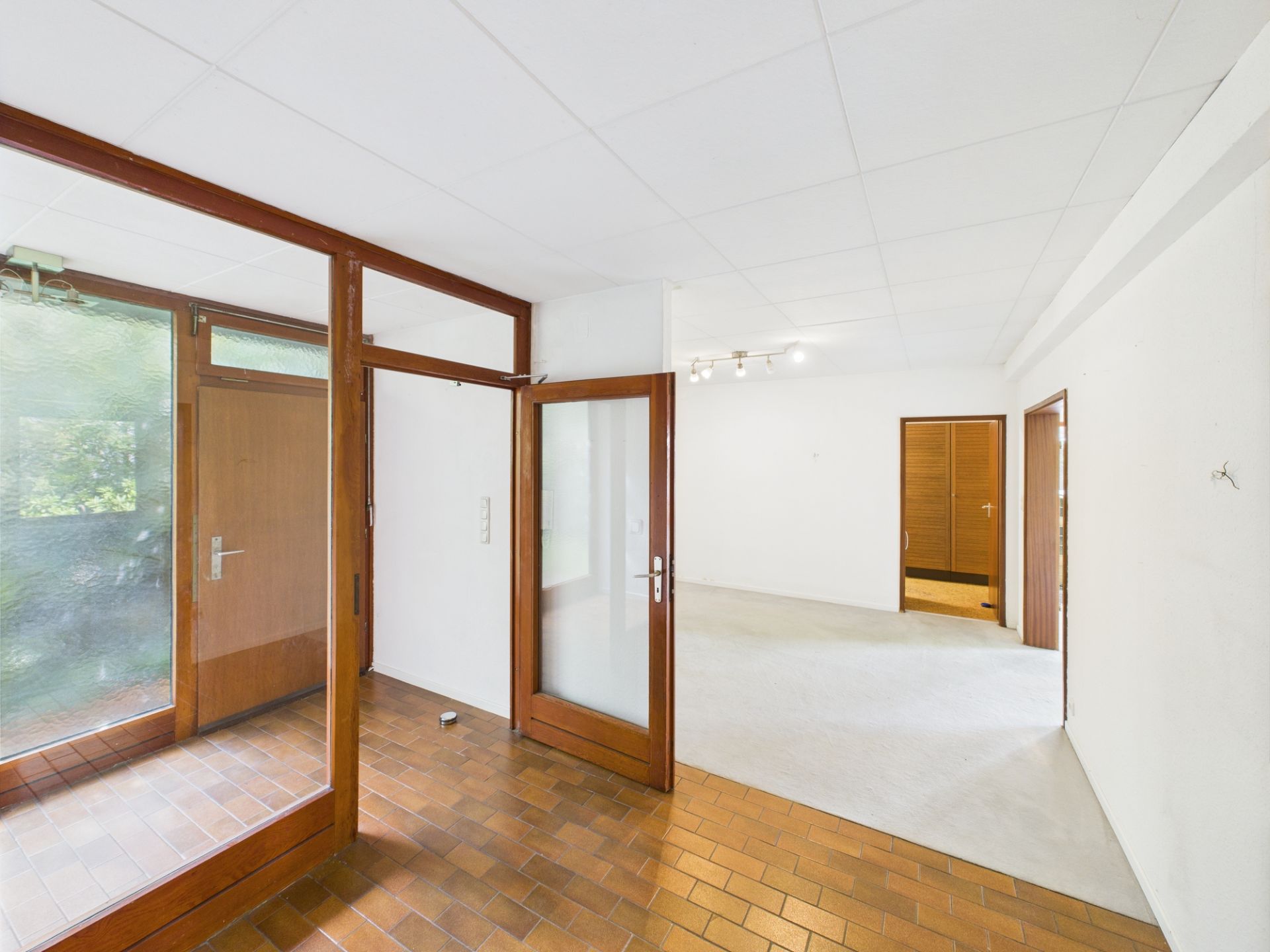 Heller Wohnungsflur mit braunen Türen, Glaselementen und Fliesenboden.