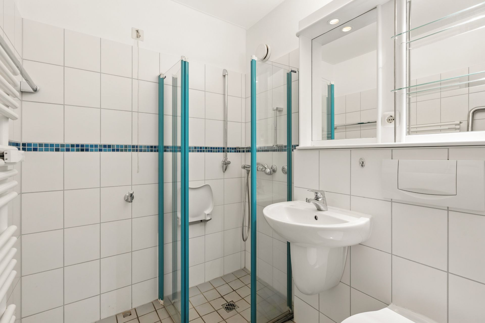 Modernes, weiß gefliestes Badezimmer mit Dusche, Waschbecken und Wandspiegel.