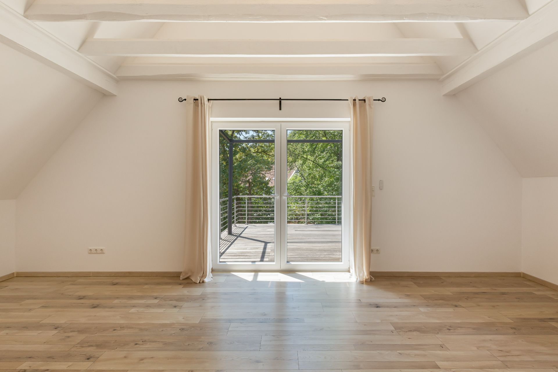 Heller, leerer Raum mit Holzboden und großen Fenstertüren zu einem Balkon.
