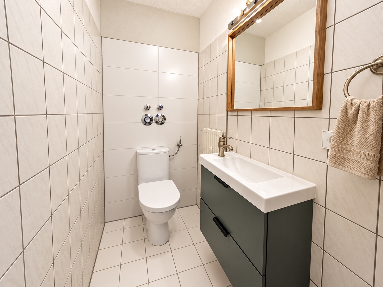 Modernes, gefliestes Badezimmer mit Toilette, Waschbecken und Spiegel.