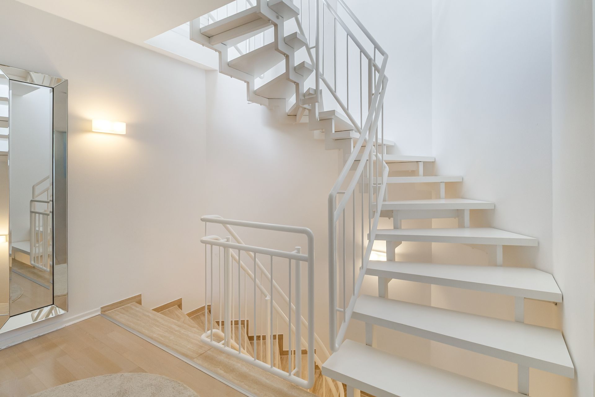 Helle Treppenhaus mit weißer Wendeltreppe, großem Spiegel und Holzfußboden.