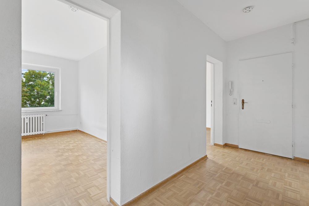Heller Flur mit Parkettboden und Blick in ein Zimmer mit Fenster und Heizkörper.