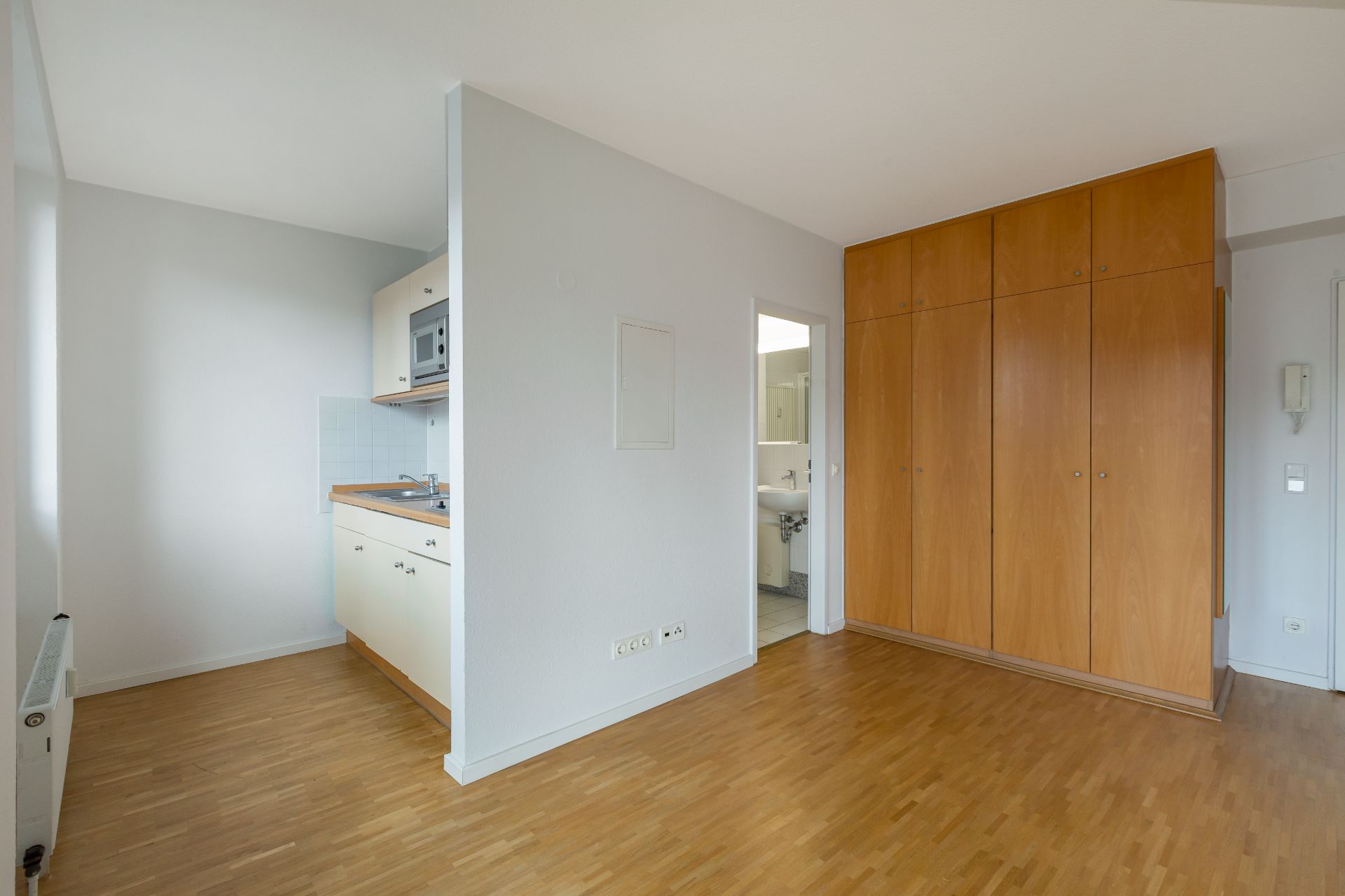 Wohnraum mit Holzboden, Einbauküche, großem Einbauschrank und Zugang zum Badezimmer.