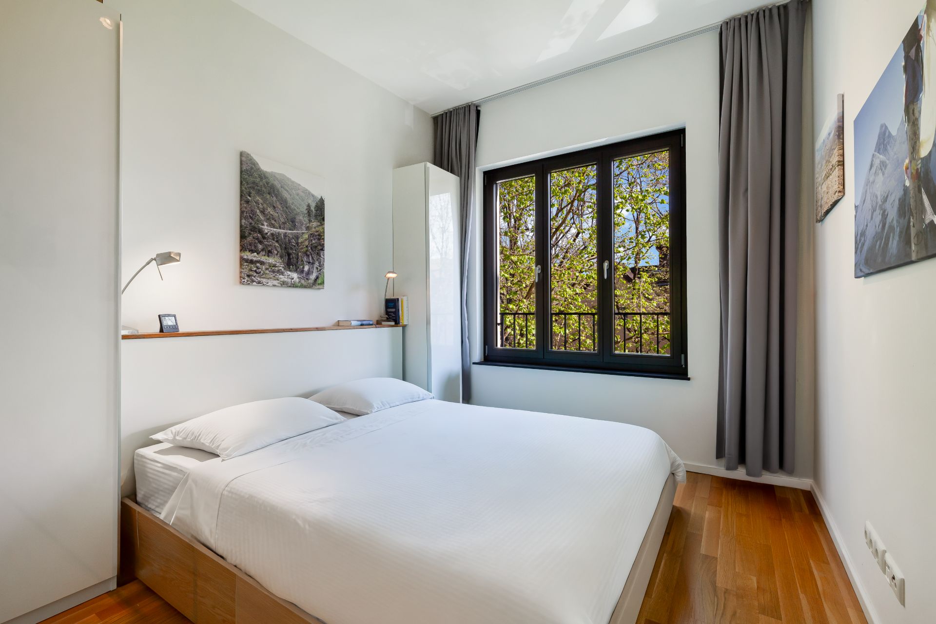 Helles Schlafzimmer mit Doppelbett, Holzfußboden und großem Fenster mit Vorhängen.