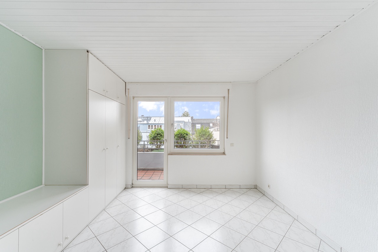 Heller Raum mit weißen Einbauschränken, Fliesenboden und Zugang zu einem Balkon.