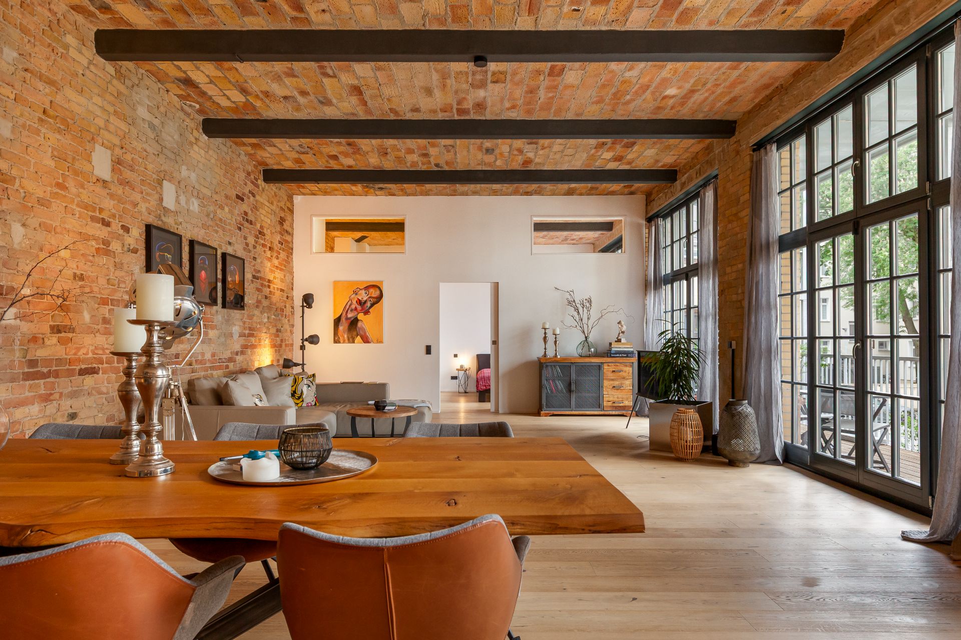 Großes Wohnzimmer mit Holztisch, Backsteinwänden und großen Fenstern.