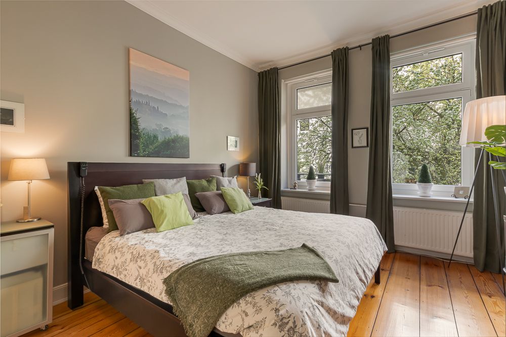 Helles Schlafzimmer mit Doppelbett, Holzboden, großen Fenstern und grünen Vorhängen.