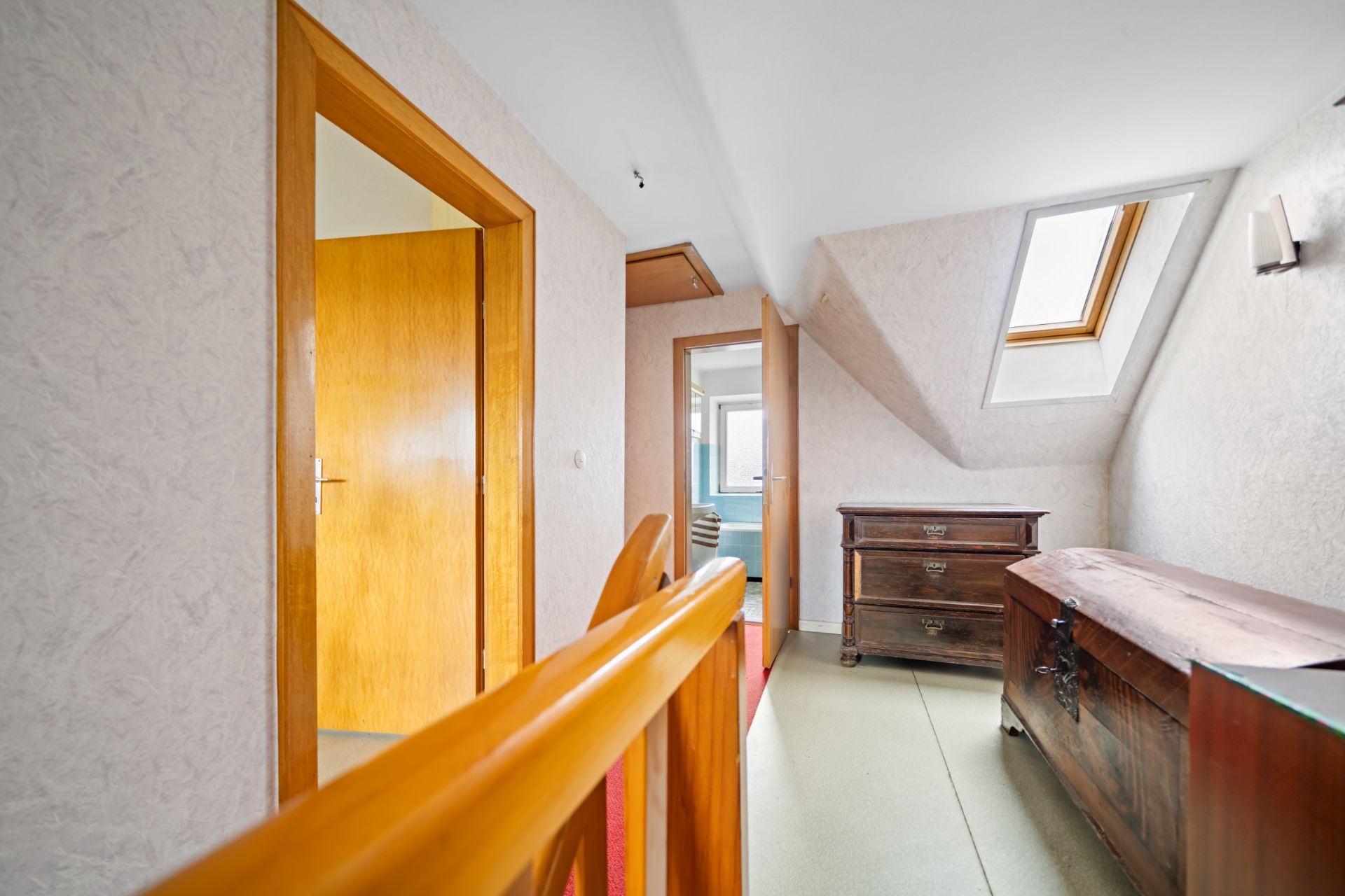 Heller Flur mit Holzgeländer, Kommode, Truhe und Dachfenster.
