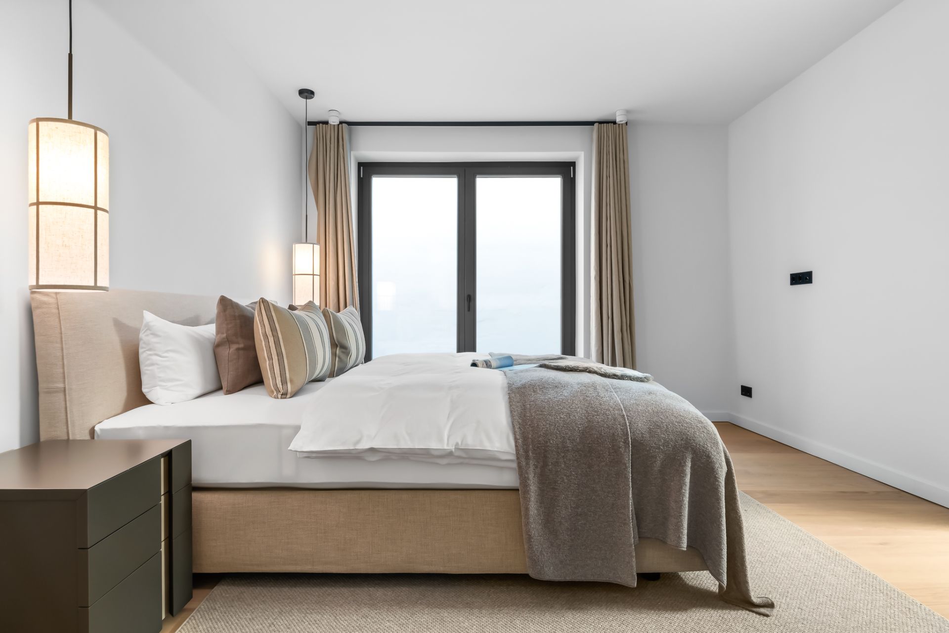 Modernes Schlafzimmer mit Doppelbett, Nachttisch, großen Fenstern und hellen Wänden.